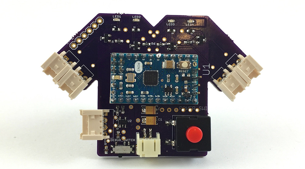 The printed circuit board is purple and in the shape of a t shirt. It has Molex connectors extending from the 'arms' of the t shirt for the conductive threads. It has a red button.