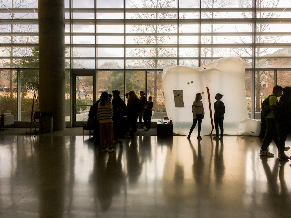 Passerby in a crowded open interior space gather round a large square translucent white inflatable.
