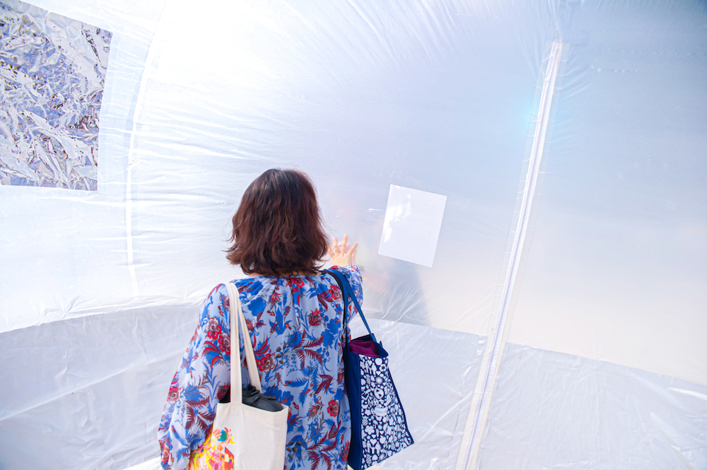 A woman inside the inflatable presses her hand against the surface of the inflatable, matching the hand press from someone outside the inflatable.