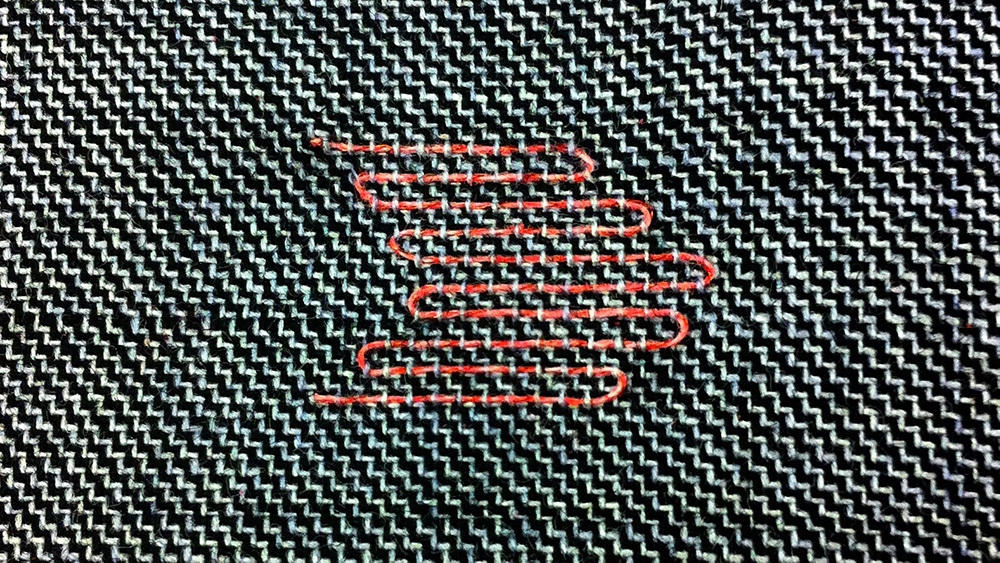 Closeup of a fabric swatch. A black and white twill weave has inlaid red thread added to it.