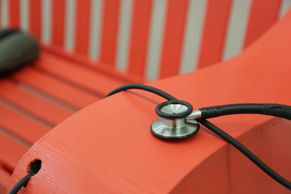 A stethoscope sits on the arm rest of the red bench.