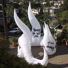 A large white inflatable sculpture about 12 feet tall wraps in a semicircle. In the background is a suburban street.