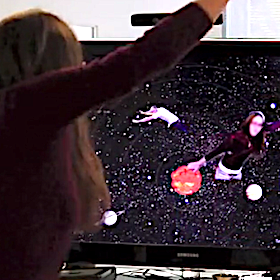 A woman (facing away from the camera) reaches her arm upward. On a screen in front of her she is shown overlaid on an image of outer space, as if she were flying through outer space. Another person is shown on the screen also flying through space in a silly arms-outstreteched position.