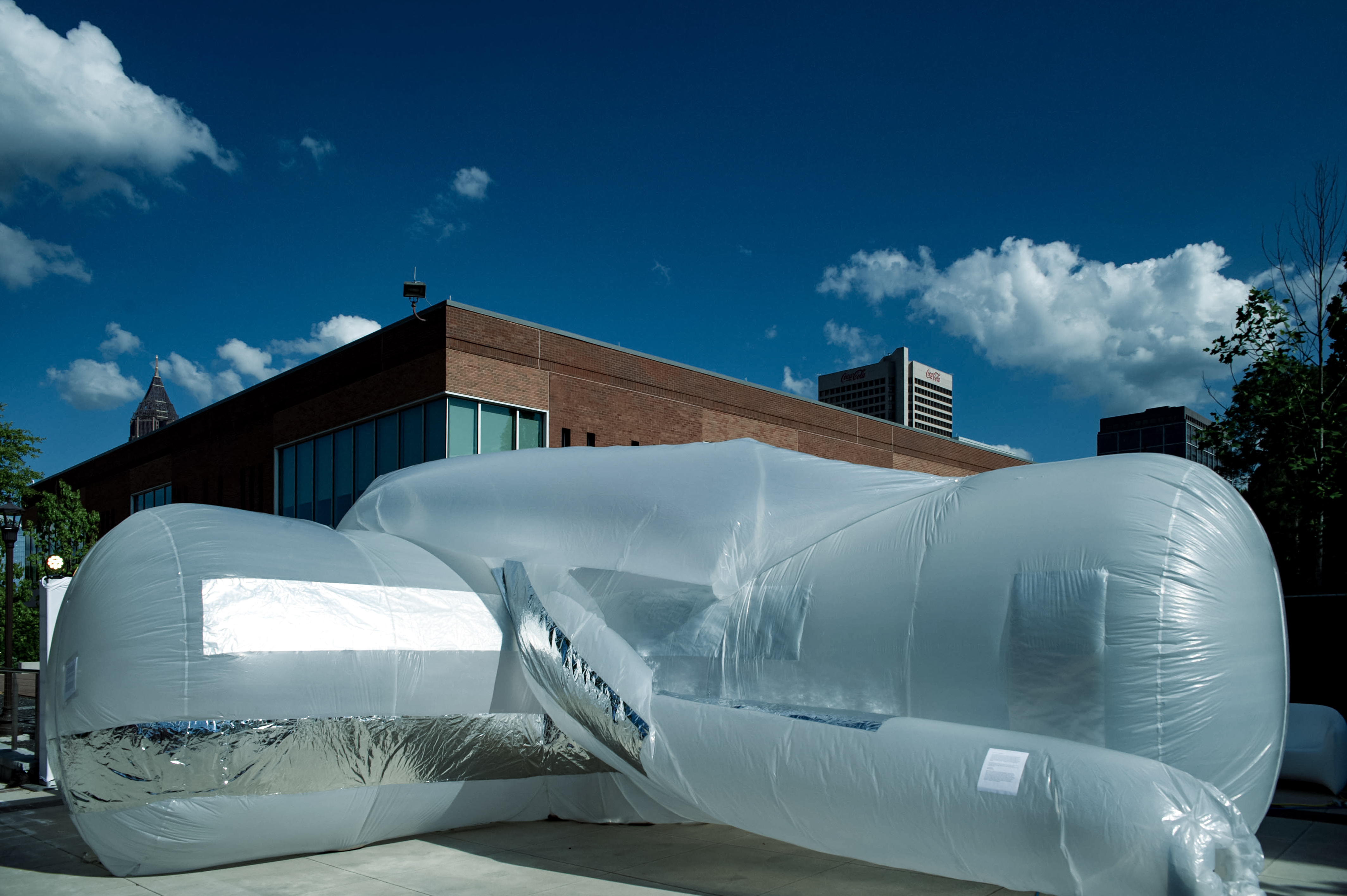 View from the outside of a large inflatable, a big tube about 8 feet in diameter. It makes a right angle bend and the viewer is in the inside of the 'elbow' angle. There are some smaller tubes twisting around the outside. The inflatable is white plastic with some stripes of silver foil