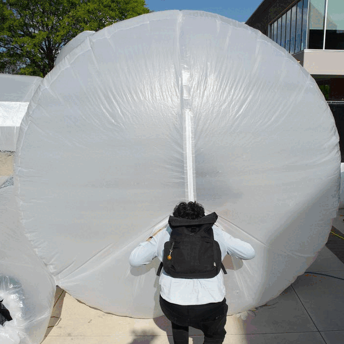 A person is seen from behind entering the inflatable through an unzipped vertical slit at the end of the tube.